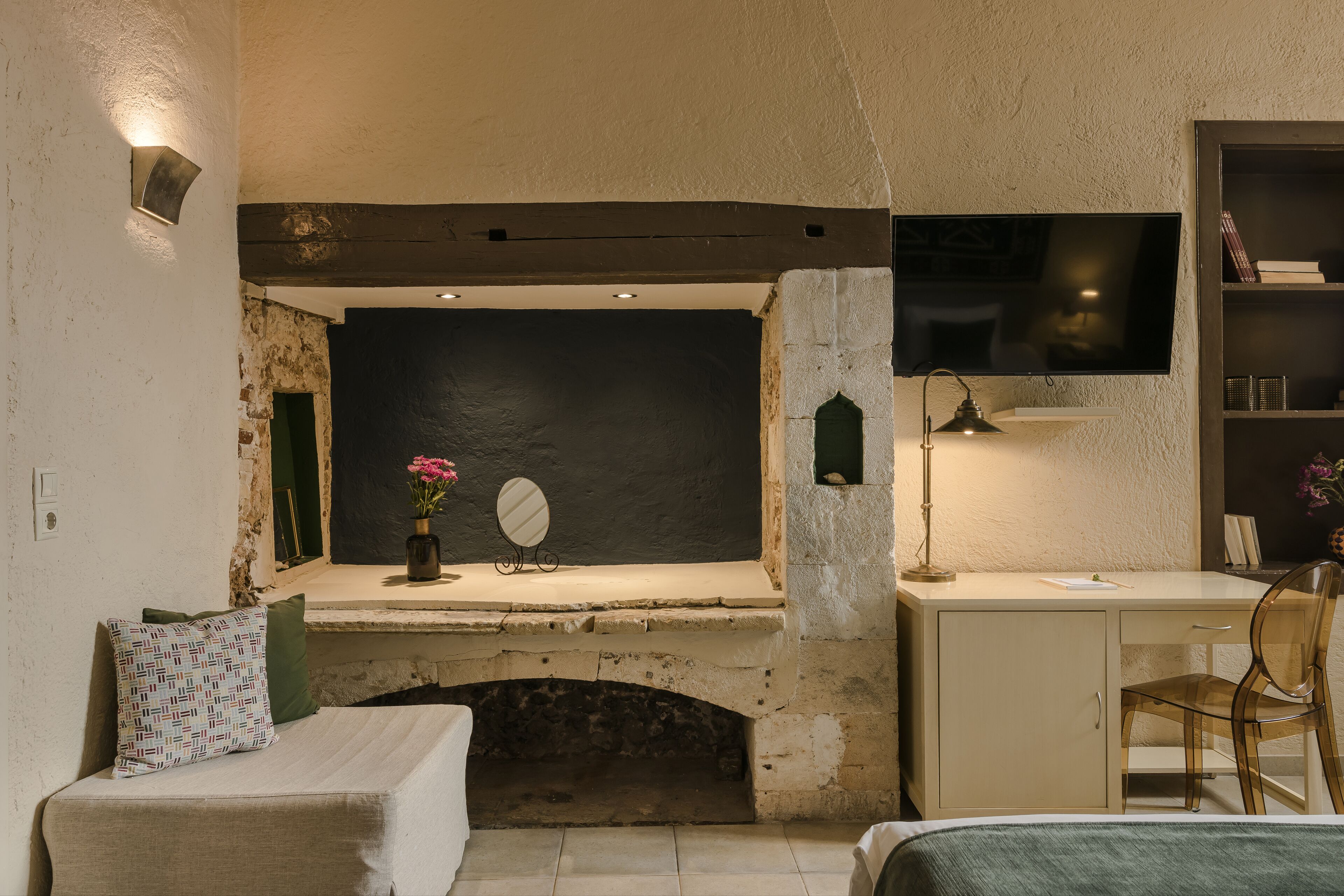 Une pièce avec une cheminée en pierre, un bureau avec une chaise, un lit et un téléviseur fixé au mur.