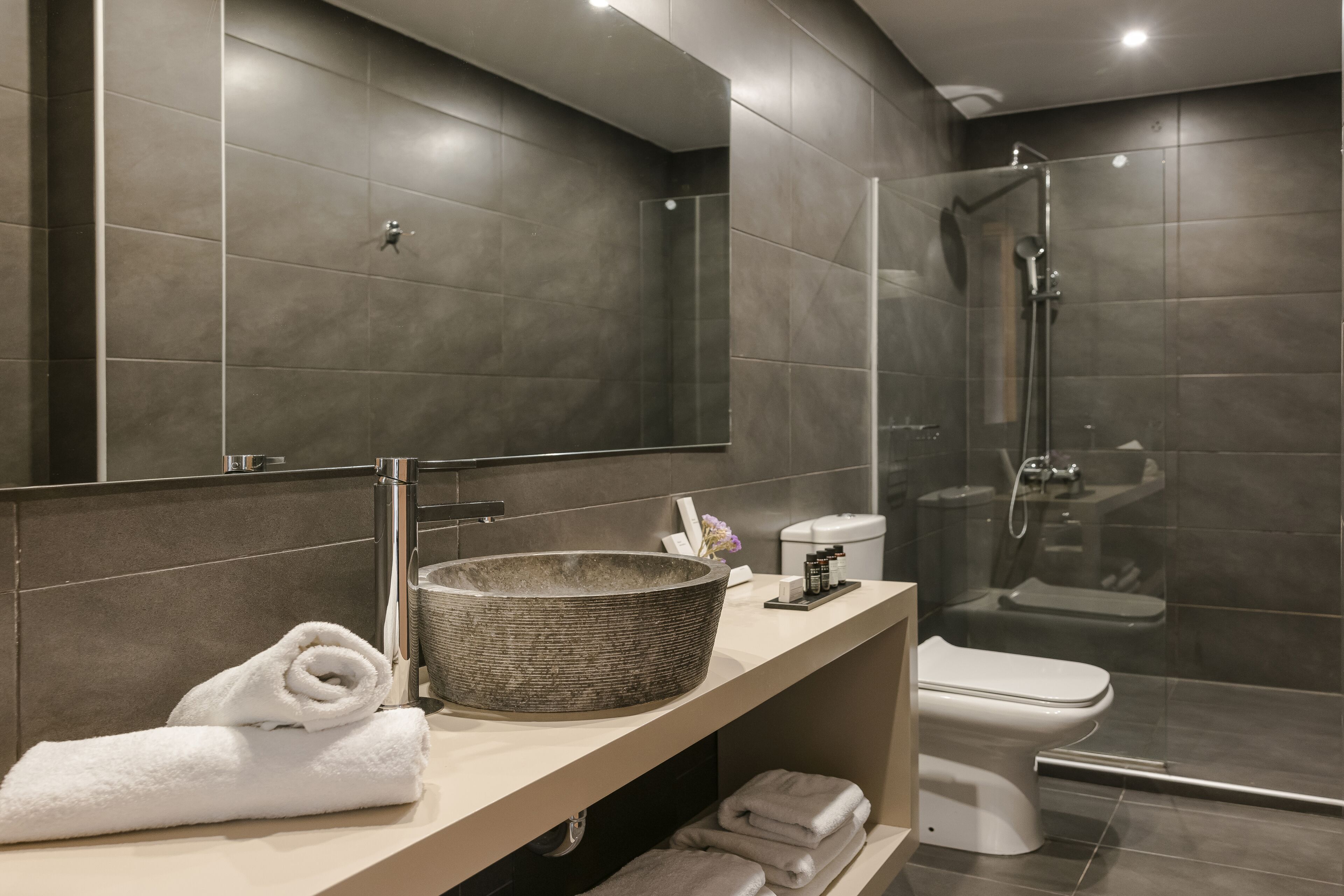 Un baño moderno con un espejo grande, un lavabo, un inodoro y una zona de ducha con mampara de cristal.