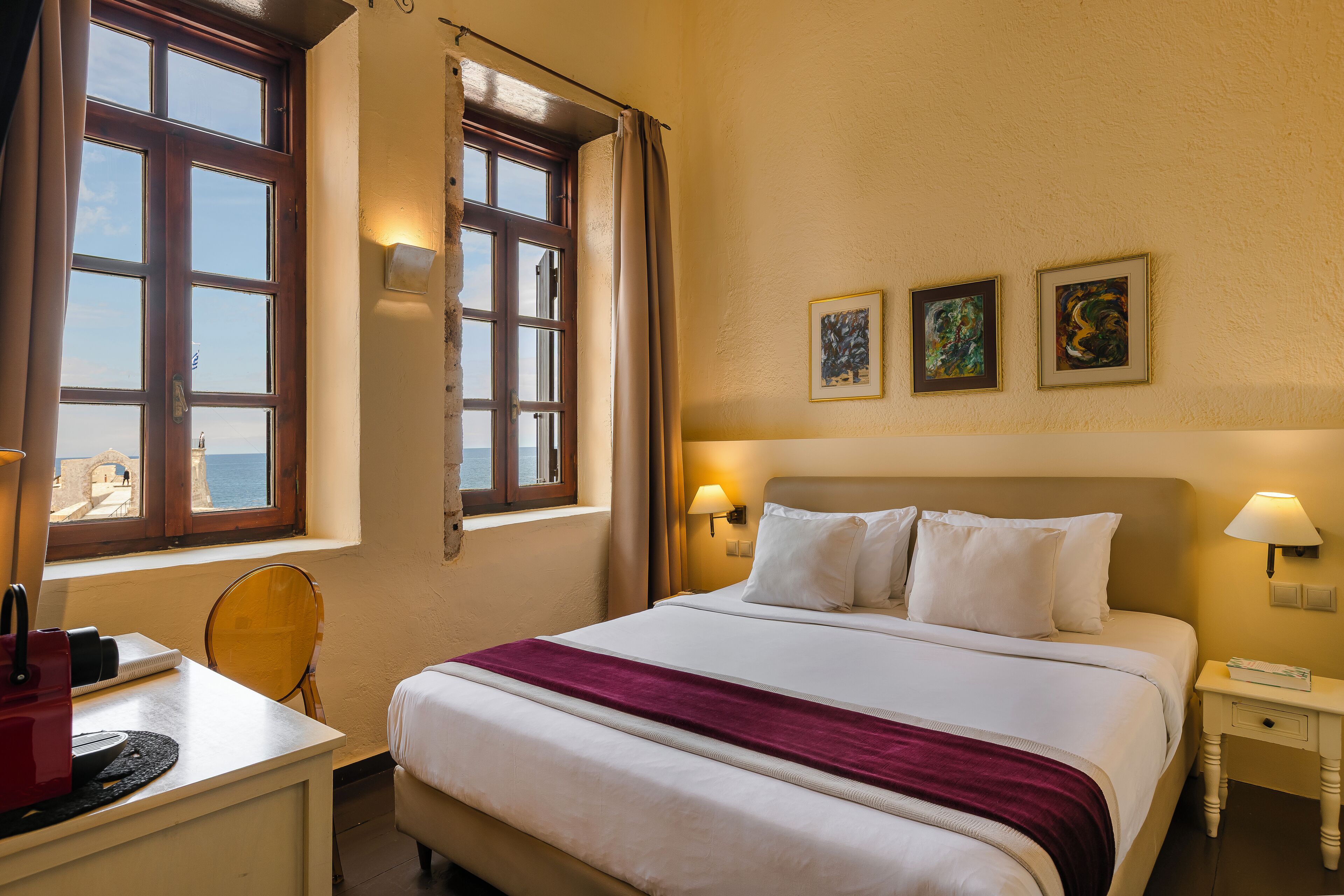 Une chambre d’hôtel avec un lit, des lampes de chevet, un bureau avec une chaise et une fenêtre avec des rideaux.
