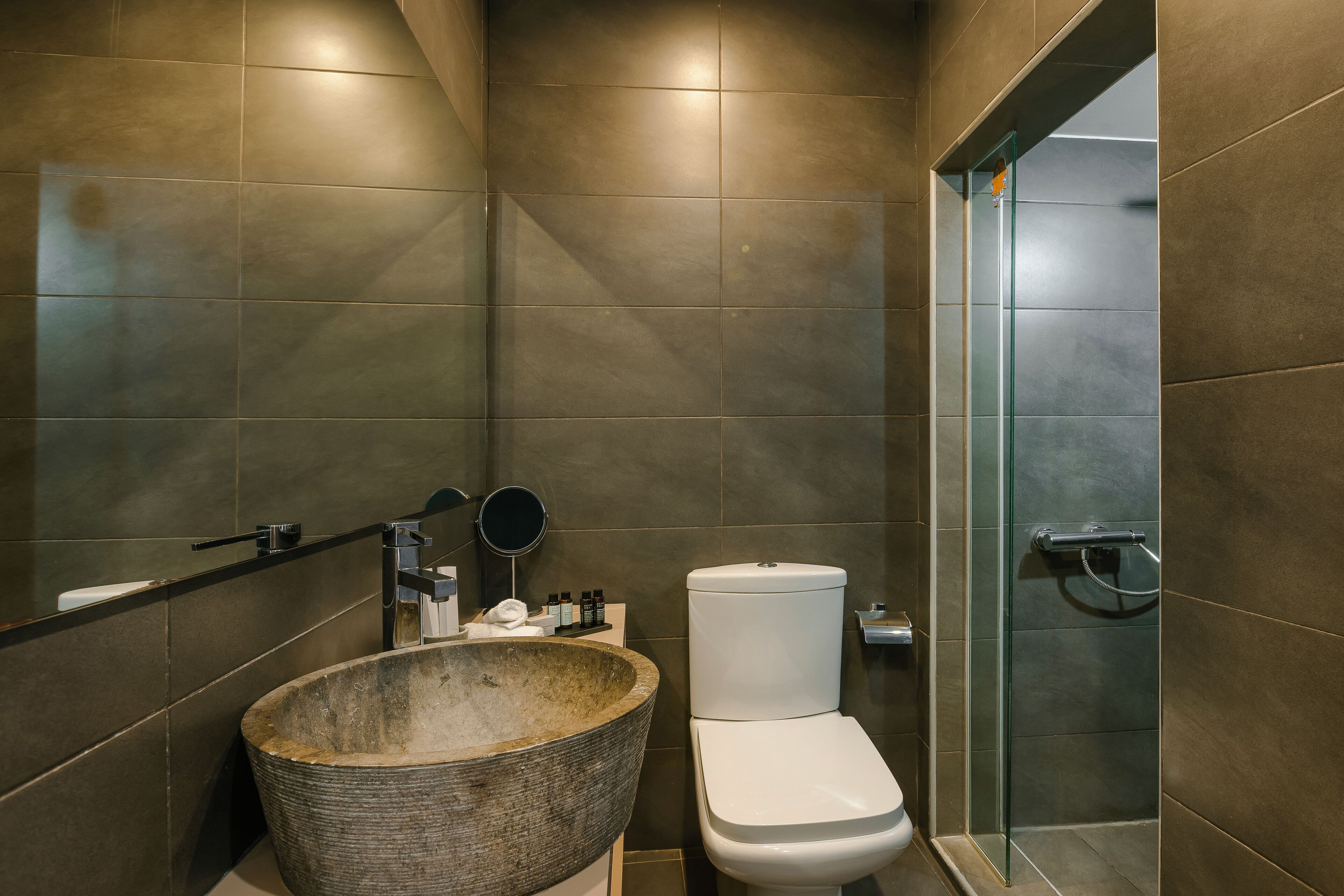 Un baño moderno con un lavamanos de piedra grande, un inodoro y una cabina de ducha de vidrio.