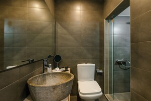 Un baño moderno con un lavamanos de piedra grande, un inodoro y una cabina de ducha de vidrio.