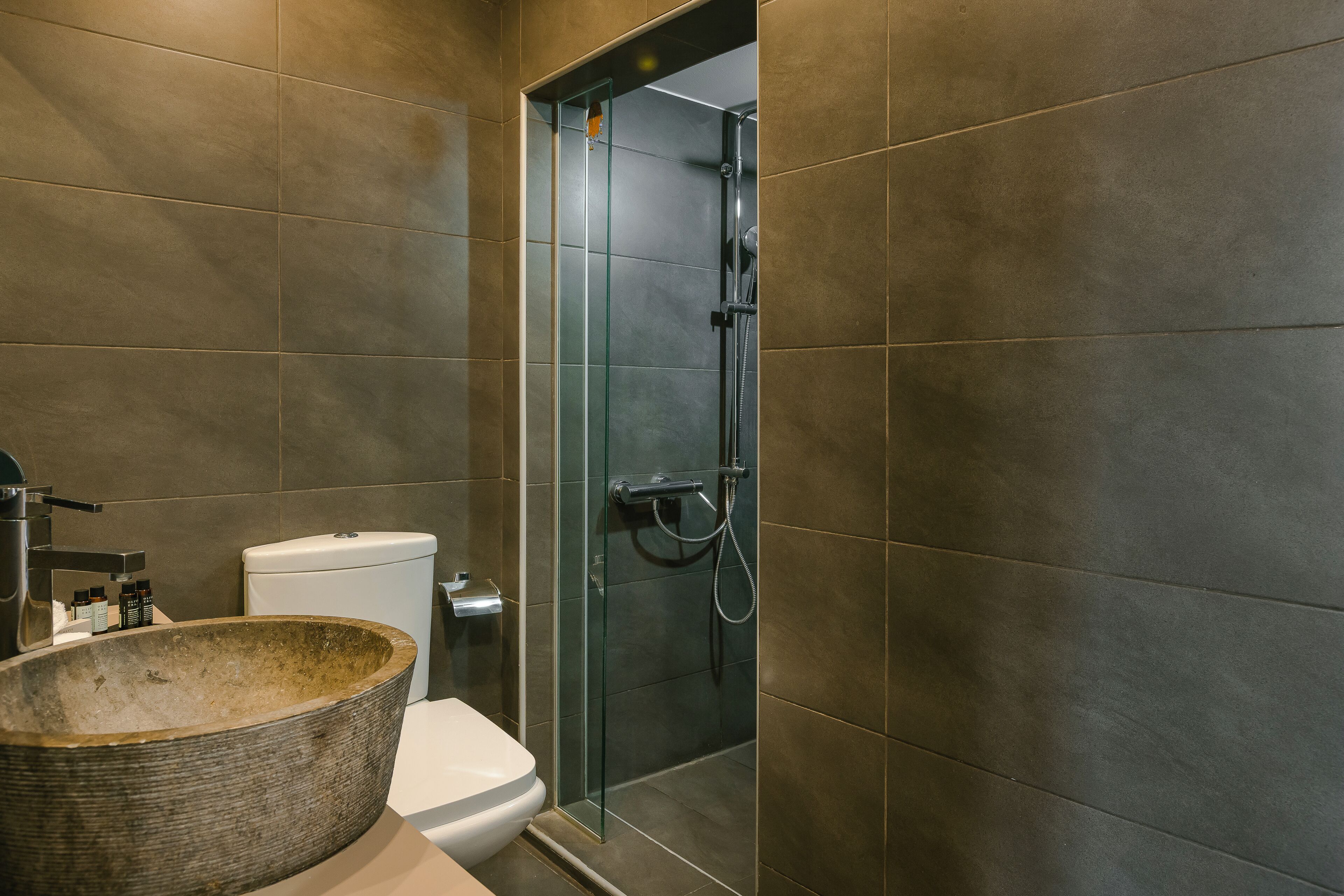 Une salle de bain moderne avec un grand lavabo en pierre, des toilettes et une douche séparée par des parois en verre.