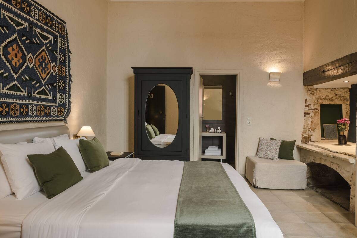 Habitación de hotel con una cama grande, un armario con espejo, una pequeña zona de estar y una chimenea.