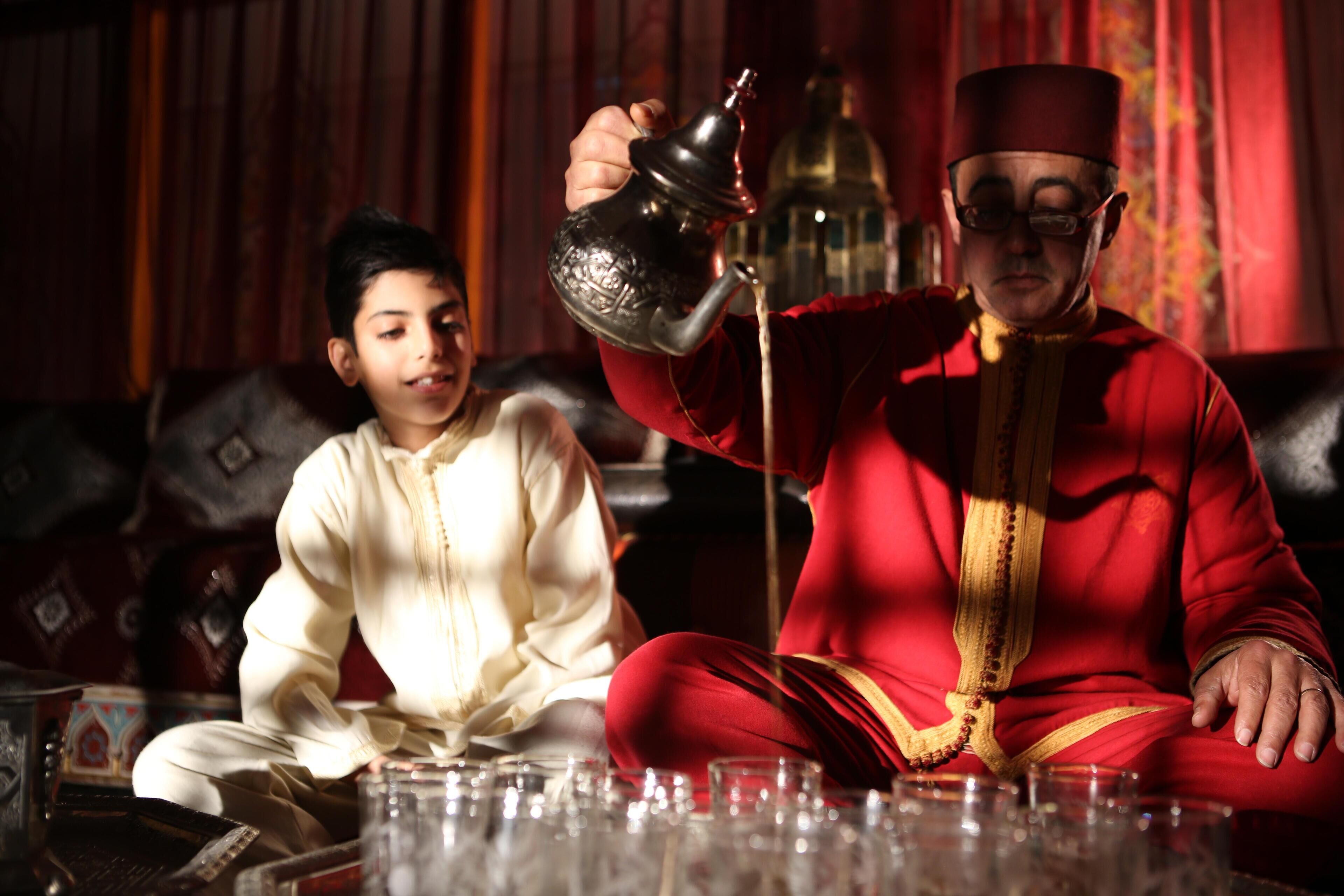 A person in traditional attire sitting on a sofa with a teapot.