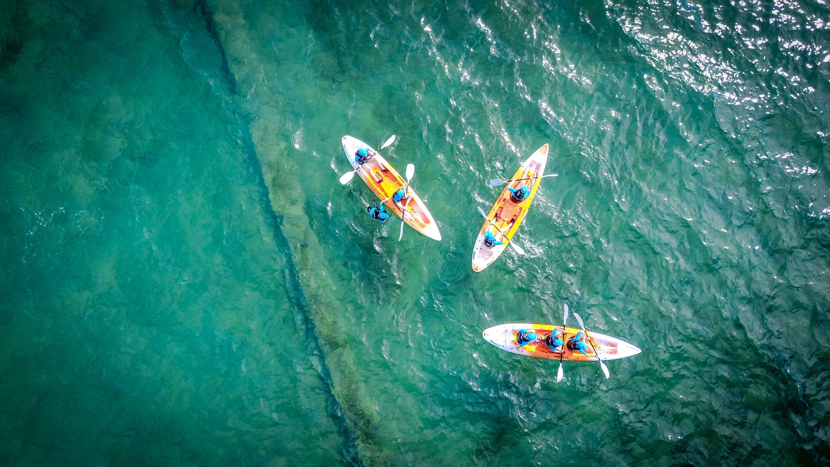An aerial view of three kayaks on clear turquoise water.