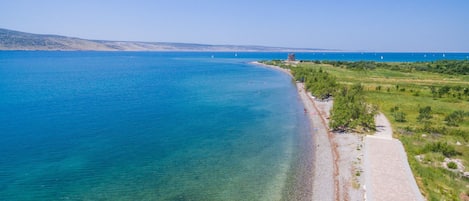 Uma estrada costeira com uma praia à direita, águas azuis cristalinas e colinas ao longe.