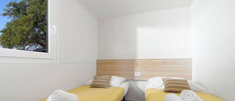 Une chambre avec deux lits, chacun recouvert d’une couvre-lit jaune et agrémenté d’oreillers blancs, et dotée d’une tête de lit en bois.