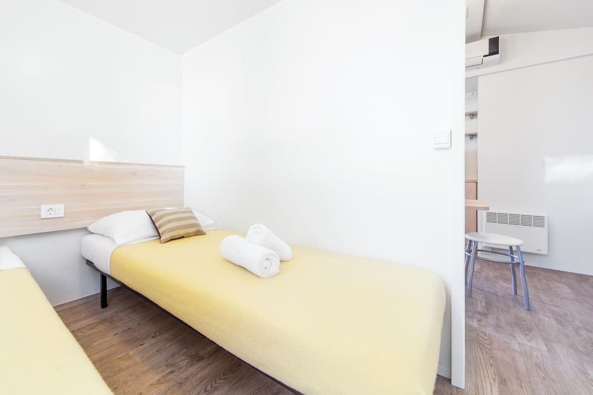 A hotel room with two single beds, a wooden headboard, a white wall, a small white table, and a radiator.
