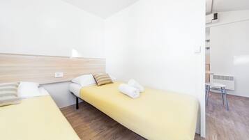 A hotel room with two single beds, a wooden headboard, a white wall, a small white table, and a radiator.