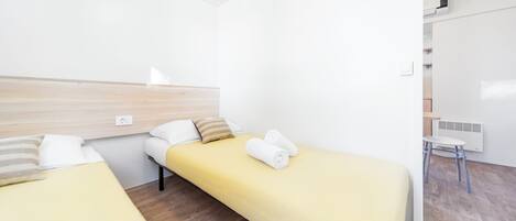 A hotel room with two single beds, a wooden headboard, a white wall, a small white table, and a radiator.