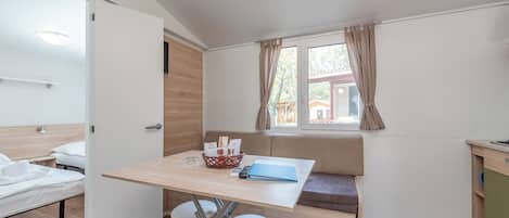 A compact room with a bed, a dining table with stools, a bench, and a window with curtains.
