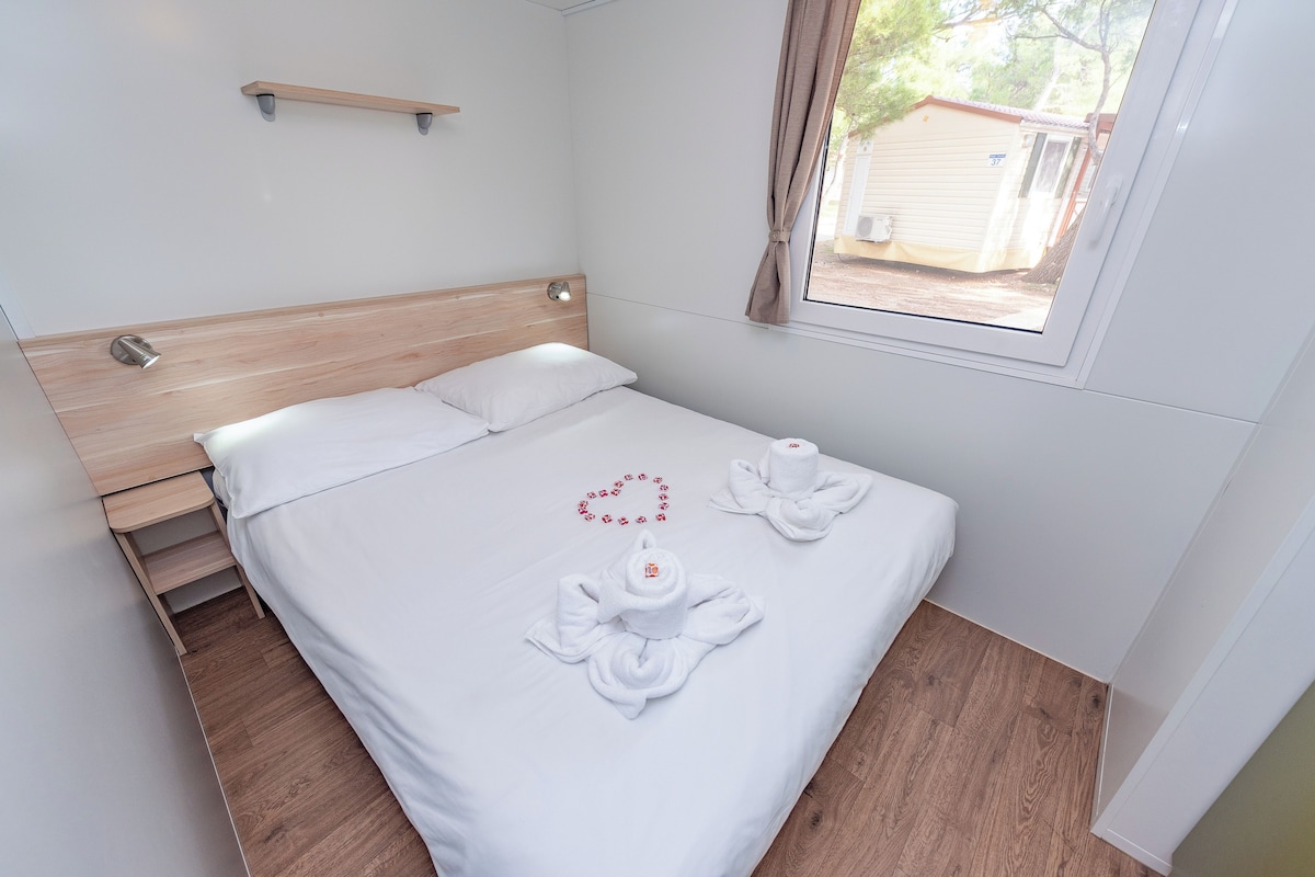 A neatly made bed with white linens and two towels arranged in a heart shape on the bed.