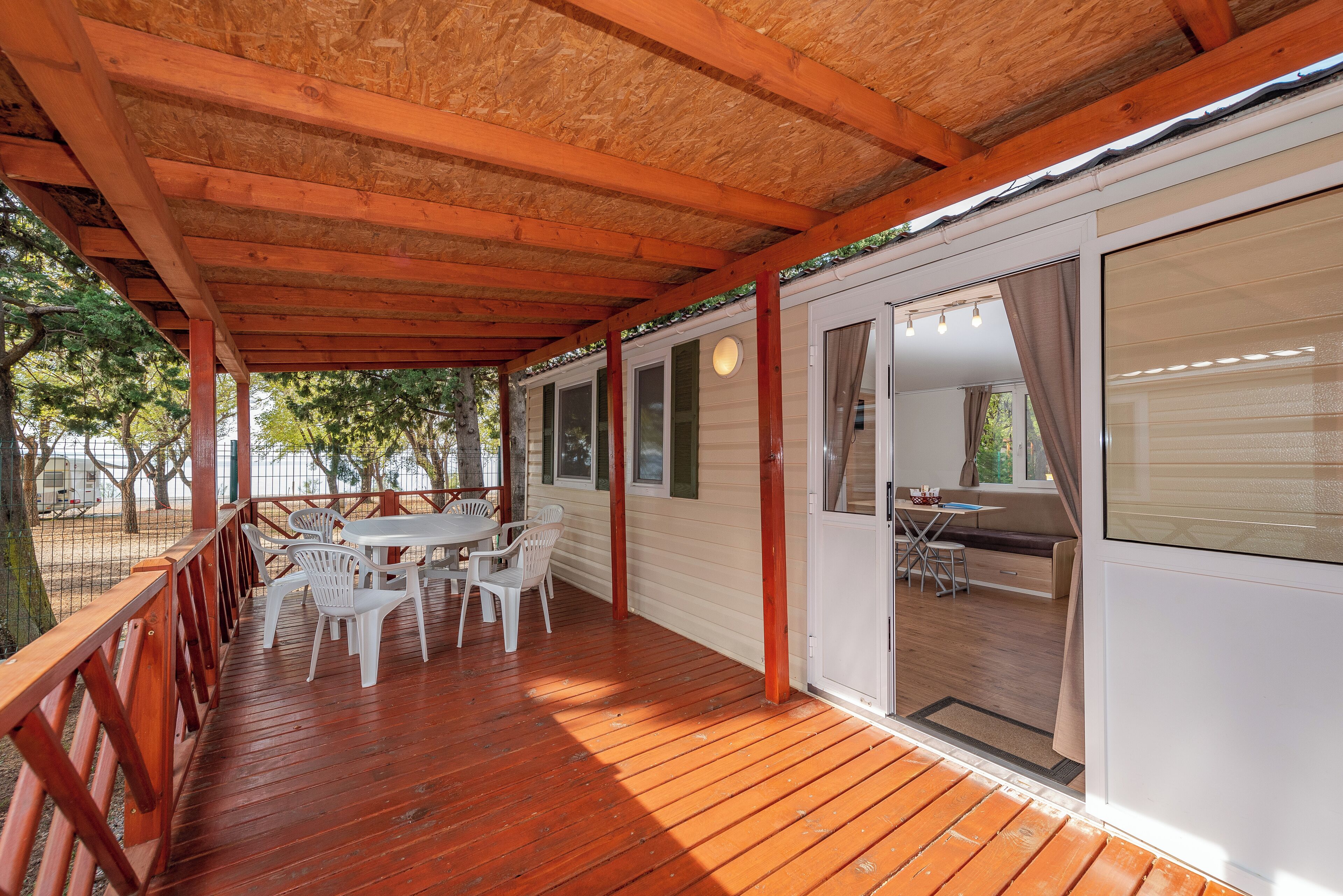 A covered outdoor area with a wooden deck, white plastic chairs, and a table.