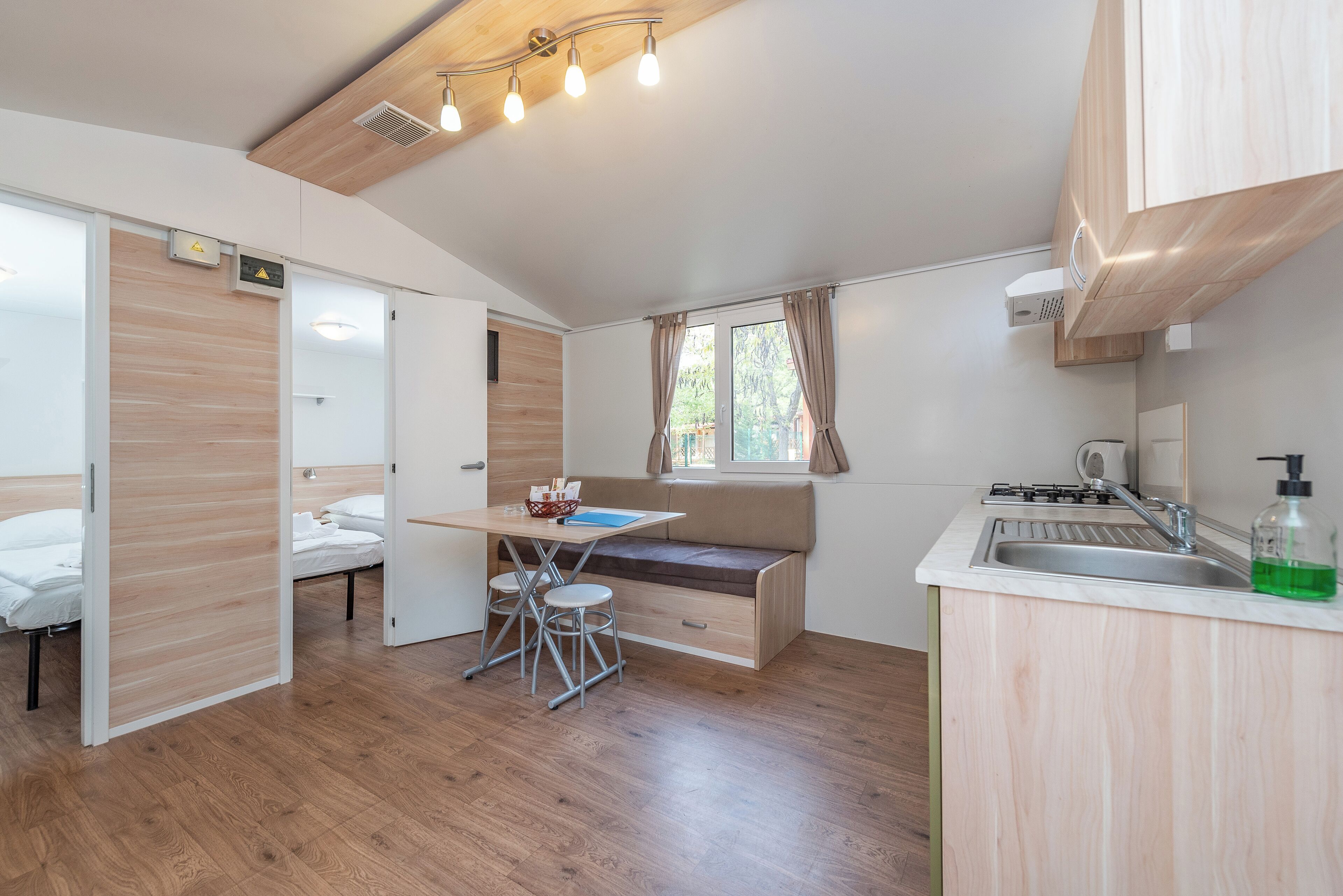 A compact kitchen with a dining area, wooden flooring, and a window with curtains.