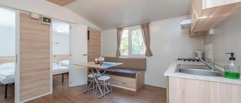 A compact kitchen with a dining area, wooden flooring, and a window with curtains.