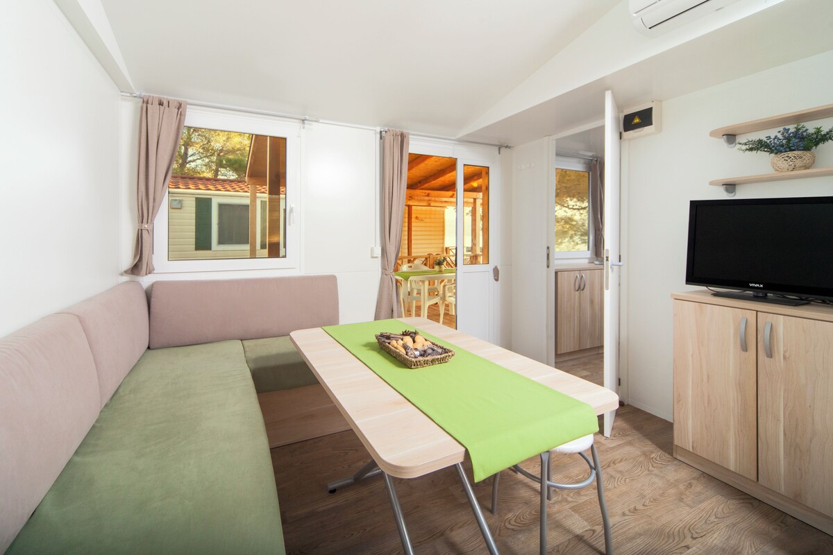 Una habitación pequeña con sofá, una mesita con bandeja, televisor en un mueble y una ventana con cortinas.