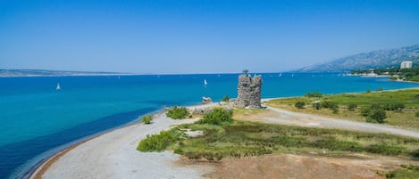 A coastal landscape with a sandy beach, a stone tower, and a clear blue sea.