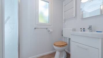 A bathroom with a white toilet, wooden floor, white cabinetry, a mirror, and a window.