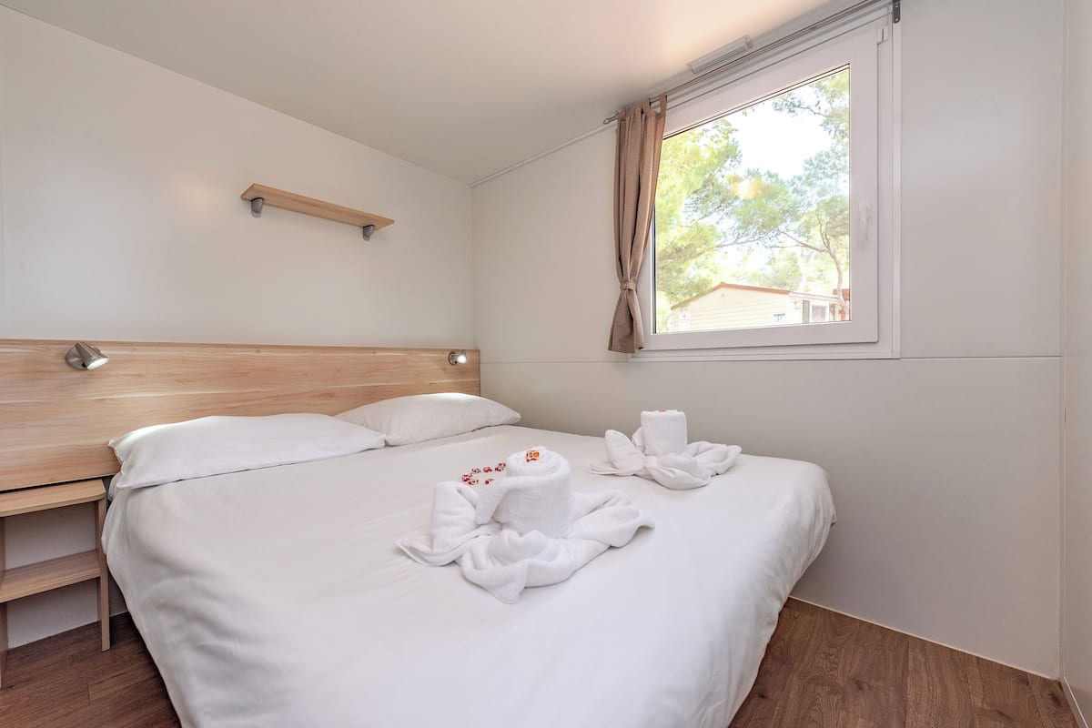A neatly made bed with white linens and towels arranged on it.