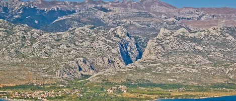 A coastal town with mountainous terrain in the background, a clear blue sea, and a small settlement with buildings.