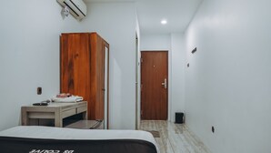 A hotel room with a bed, a wooden wardrobe, a desk with a chair, a small table, and a door leading to another room. - DS Residence Siliwangi (Semarang)