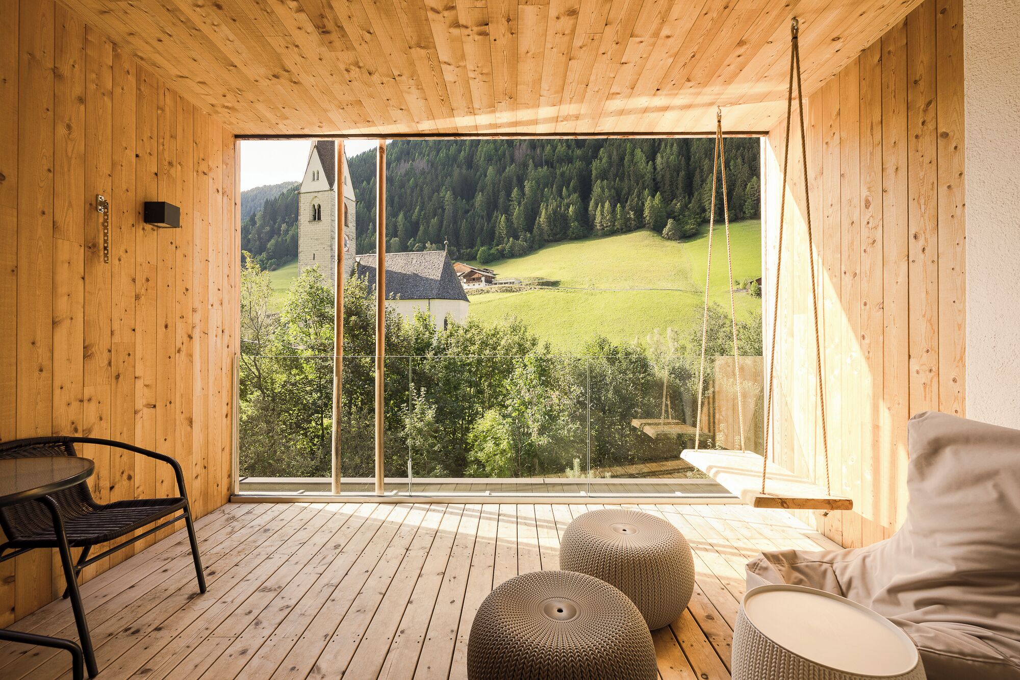Ein Holzinnenraum mit einem großen Fenster mit Blick auf eine grüne Landschaft und einem Steinturm.