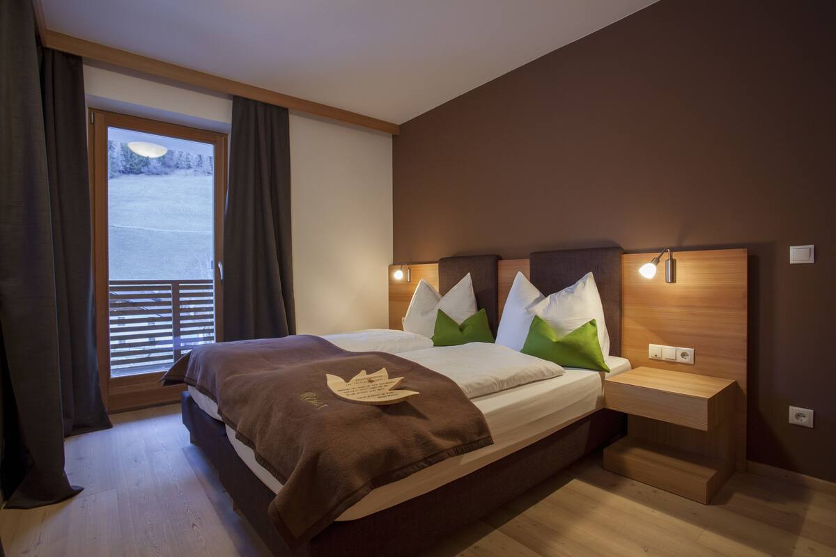 A bedroom with a large bed, a nightstand, a window with curtains, and a view of a snowy landscape.