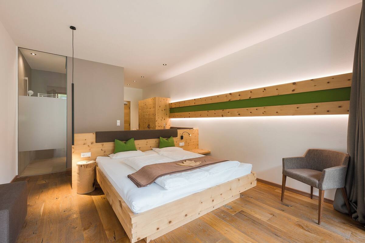 A modern bedroom with a wooden bed, green pillows, a wooden nightstand, a chair, and a mirror.