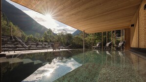 An infinity pool with clear water reflecting the sky and mountains, wooden deck chairs, and a view of a mountainous landscape. - Naturhotel Rainer (Racines)