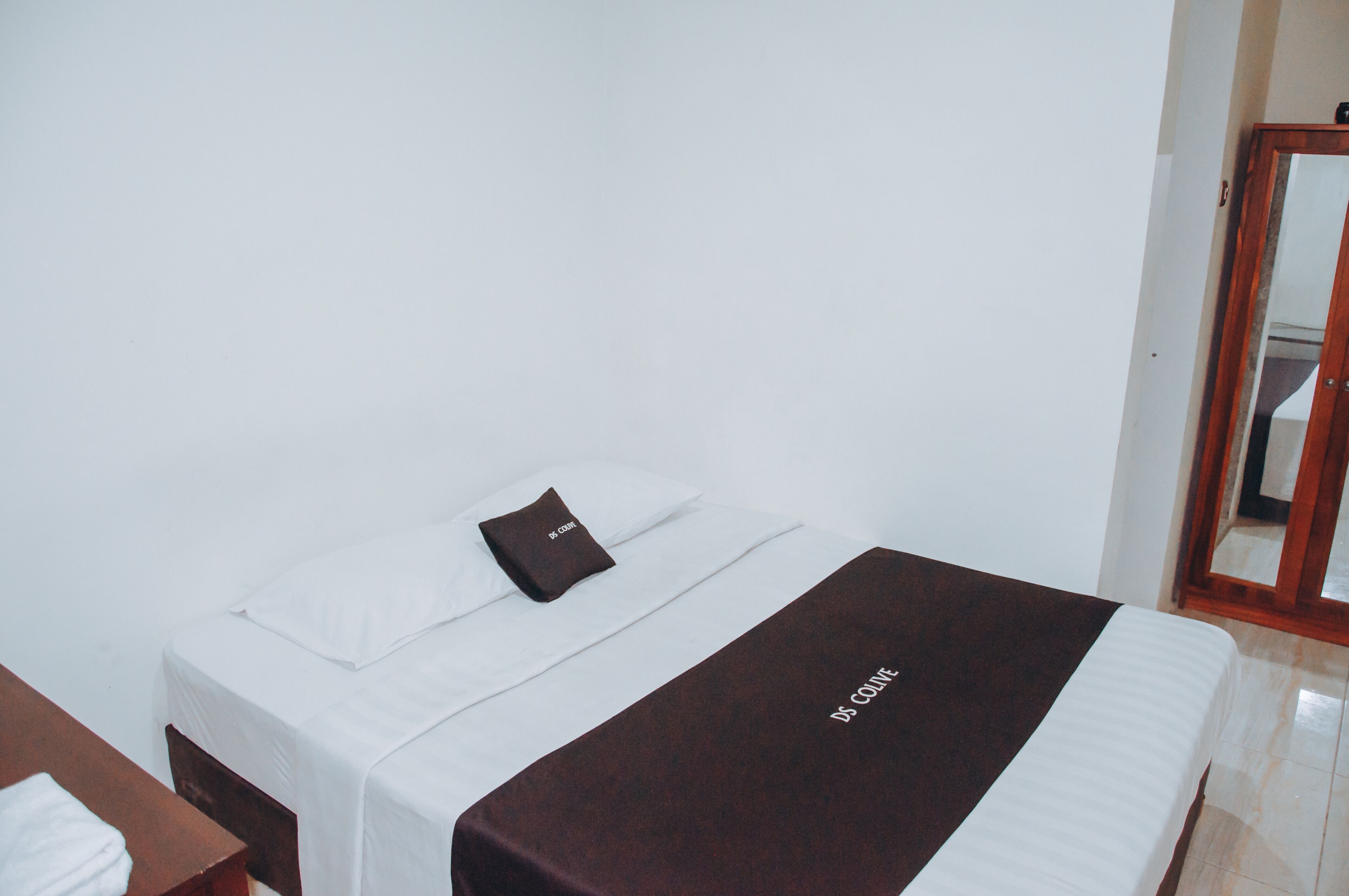 Una cama individual con colchón blanco, manta marrón y una almohada pequeña de color café.