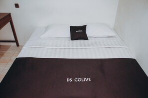 A bed with a white bedspread and a dark brown blanket with "DS COLIVE" text. - DS Residences Peterongan (Semarang)