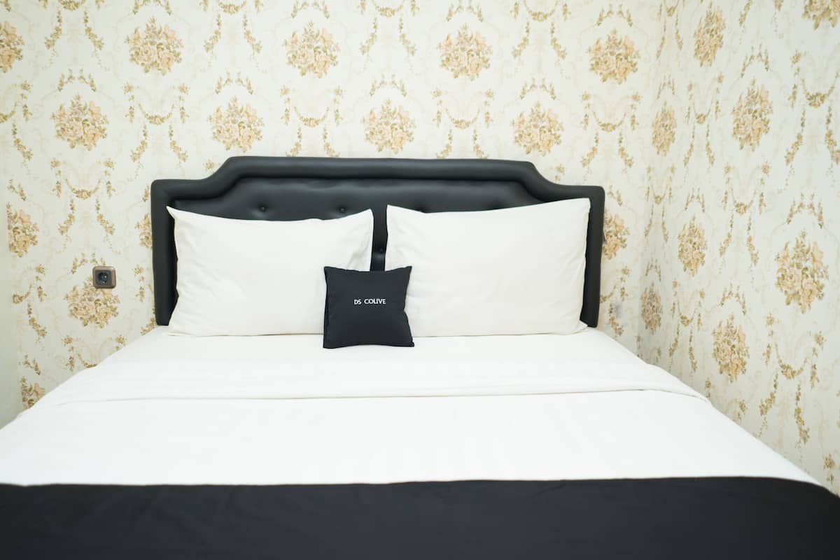 Un lit bien fait, avec une tête de lit noire et du linge de lit blanc, placé devant un mur recouvert d’un papier peint à motifs floraux.