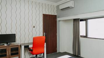 A hotel room with a desk, chair, bed, and an air conditioning unit.