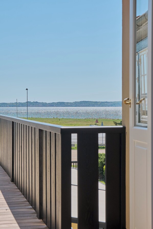 Une vue depuis un balcon doté d’une balustrade, donnant sur une étendue d’eau et une côte lointaine.