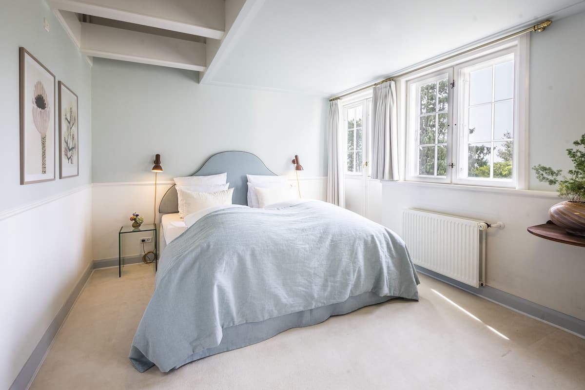 A bedroom with a bed, bedside tables, a radiator, and a window with curtains.