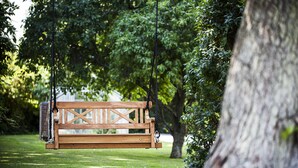 Un banc en bois, suspendu par des cordes dans un parc, avec le tronc d’un arbre sur la droite.