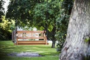 Un banco de madera colgado con cuerdas en un parque, con el tronco de un árbol a la derecha.