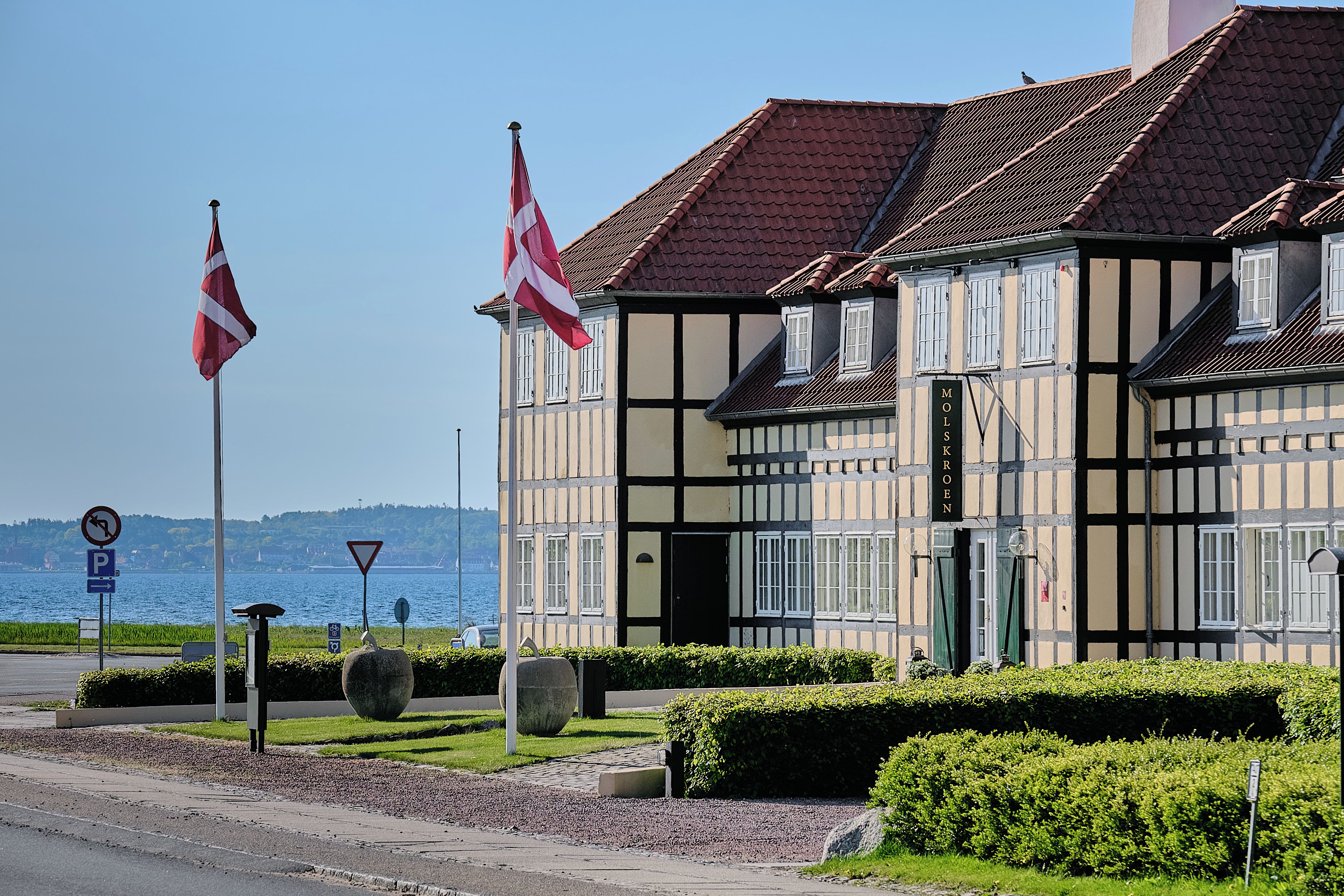 A traditional half-timbered building with a flag, a sign indicating a no parking zone, and a view of the water.