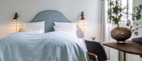 A bed with a light blue bedspread and white pillows, flanked by two wall-mounted lamps.