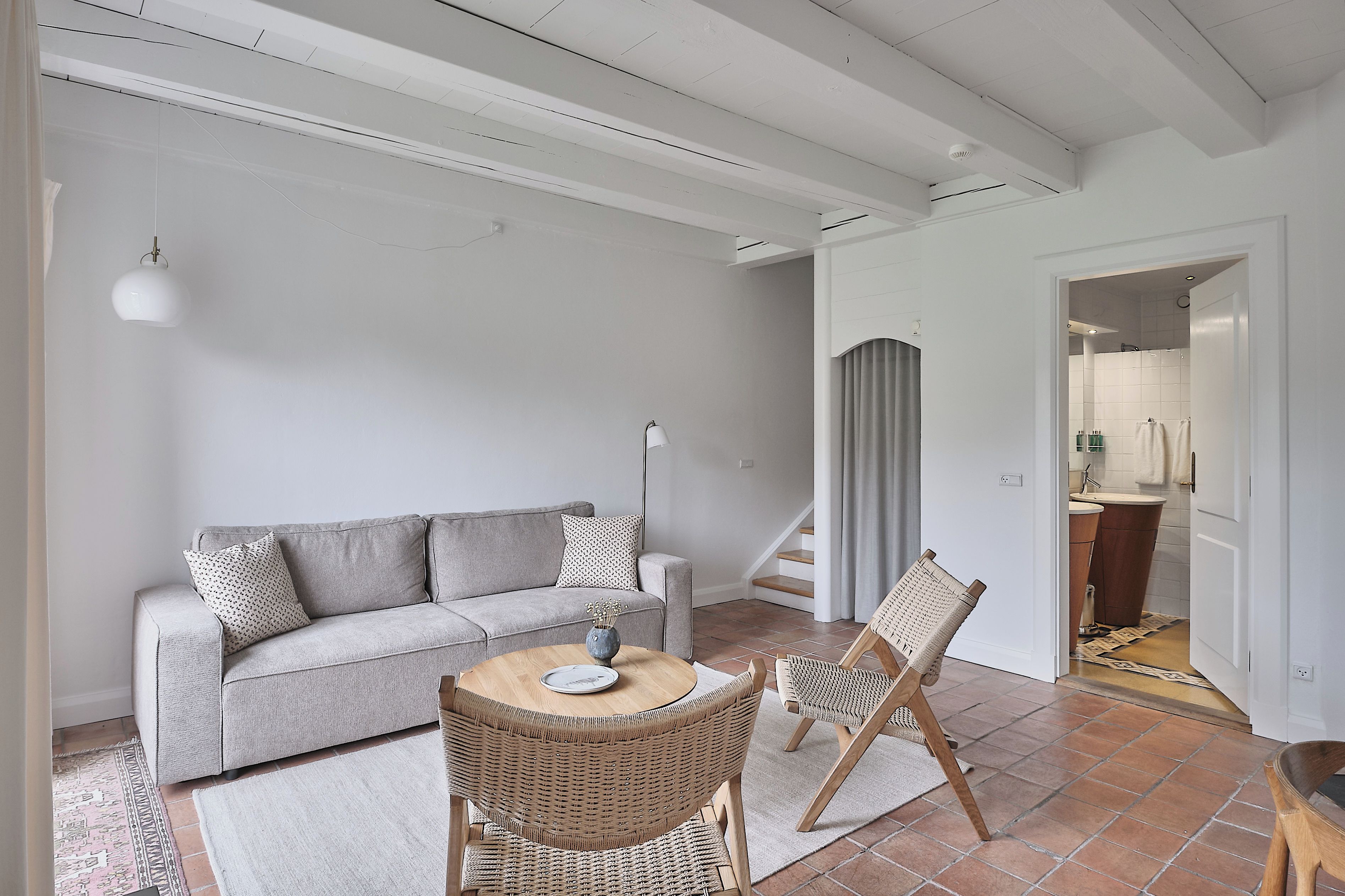 A modern living room with a grey sofa, a round wooden table, and wicker chairs.