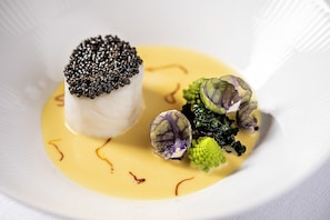 A white plate with a white fish topped with black caviar, green broccoli, and purple cauliflower.