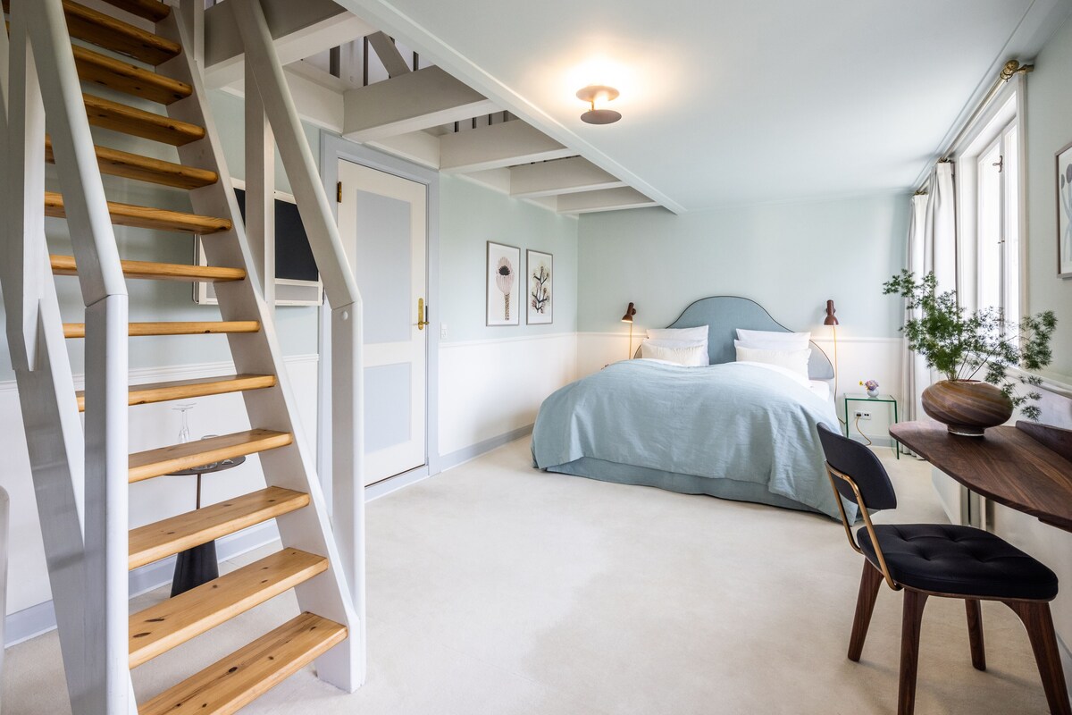 Une chambre à coucher avec un lit, une chaise, une table, une lampe et un escalier.