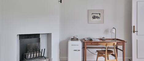 A room with a fireplace, a desk with a chair, a door, and a framed picture on the wall.