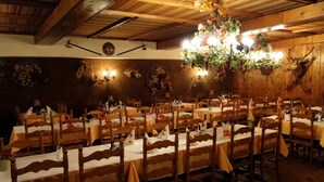 Un restaurant avec des tables et des chaises en bois, un lustre et des trophées de cerf accrochés aux murs.