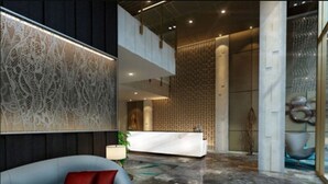 A modern lobby with a reception desk, a grey sofa with cushions, and a patterned wall. - Louis Kienne Hotel Simpang Lima (Semarang)