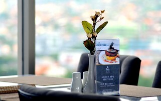 A dining table with a menu stand, a vase with flowers, and a view of the city through a window.