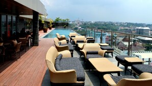 A rooftop lounge with wicker furniture and a pool overlooking a cityscape. - Louis Kienne Hotel Simpang Lima (Semarang)