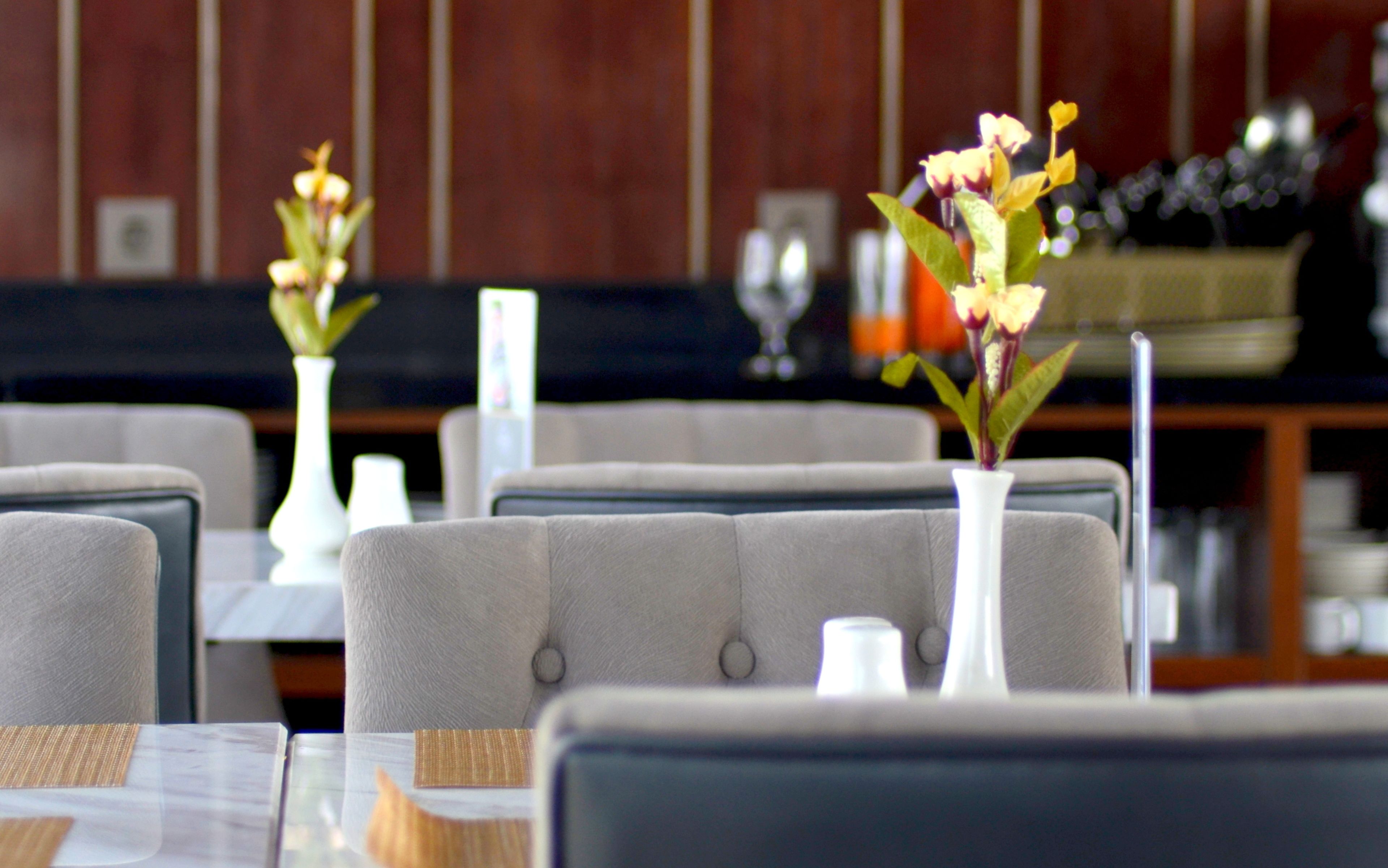 L’intérieur d’un restaurant avec des banquettes, des vases blancs ornés de fleurs et un bar en arrière-plan.
