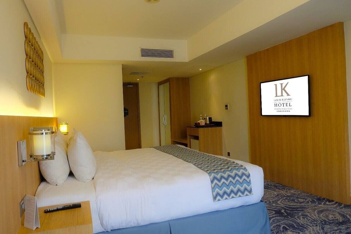 A hotel room with a bed, bedside table, lamp, and a sign indicating the hotel name.
