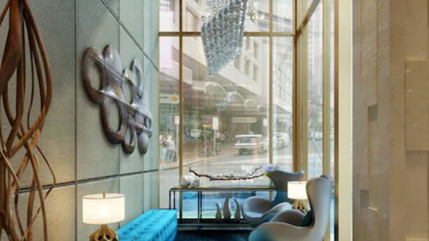 A modern lobby with a blue sofa, two armchairs, a small table with a lamp, and a decorative wall piece. - Louis Kienne Hotel Simpang Lima (Semarang)